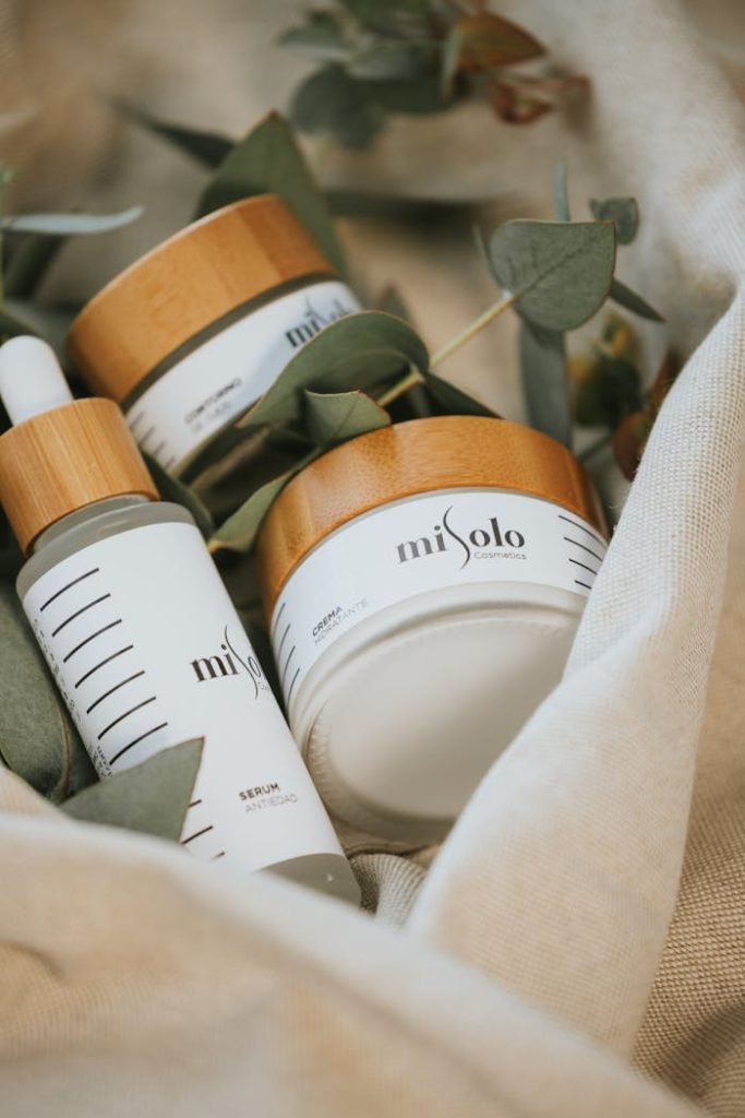 Close-up of natural skincare products with wooden caps among linen fabric and leaves.